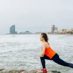 A woman stretches by the ocean in Barcelona, showcasing health and fitness by the sea.
